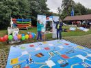Zdjęcie przedstawia 2 osoby, kobietę i mężczyznę rzucających do siebie wielką piankową kostką do gry, na pierwszym planie, wielkoformatowa gra planszowa, z tyłu kajaki i wiata