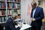 Zdjęcie przedstawiające 2 Panów jeden podpisuje książkę
