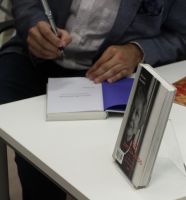 Zdjęcie przedstawia pisarza wpisującego autograf do książki