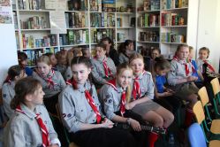 Grupa dzieci siedzi na krzesłach w bibliotece