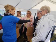 Ludzie pod namiotem siedzą na krzesłach. Jedna osoba stoi i mówi przez mikrofon.
