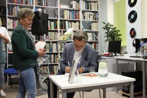 Zdjęcie przedstawia autora wpisującego autograf do książki w bibliotece