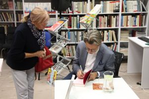 Zdjęcie przedstawia autora wpisującego autograf do książki w bibliotece