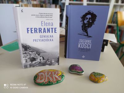 Dwie książki, pierwsza Eleny Ferrante Genialna przyjaciółka, druga Zbieranie kości Jesmyn Ward i 3 kamienie z namalowanym napisem DKK