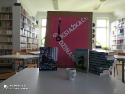 Zdjęcie przedstawia książki, kubek i plakat DKK z hasłem Godzinami o książkach
